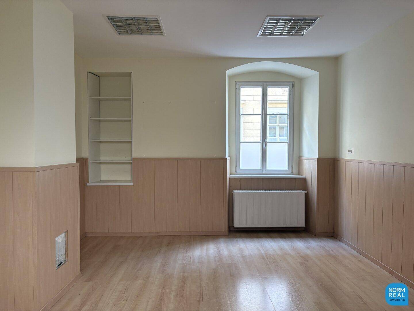 Gewerberaum mit einem Fenster, Einbauregal und Holzpaneelen an den Wänden.