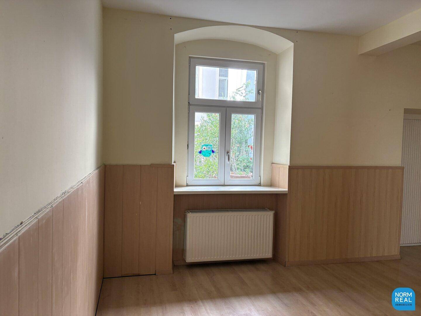 Heller Gewerberaum mit einem Fenster, Heizkörper und Holzpaneelen an den Wänden.