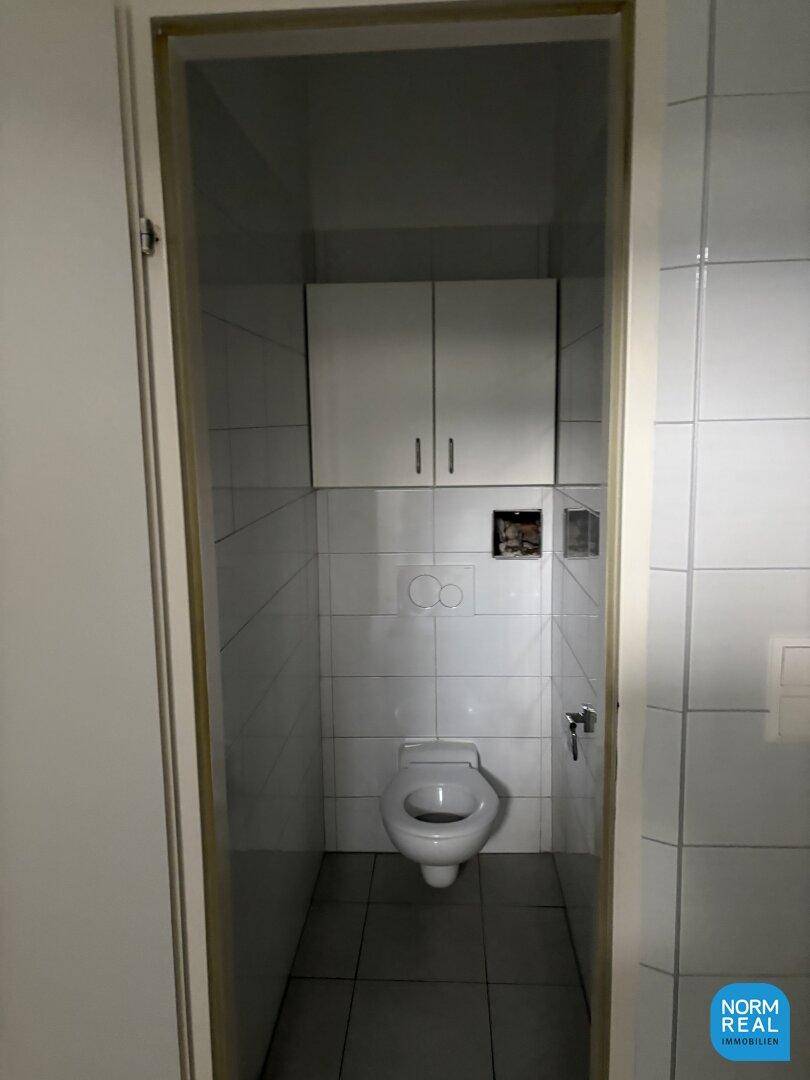 Schmale Toilette mit Wand-WC, Fliesenboden und weißen Wandschränken für Stauraum.