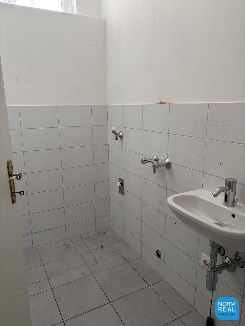 Gefliester Raum mit Waschbecken und Armaturen, bereit für weitere Installationen.