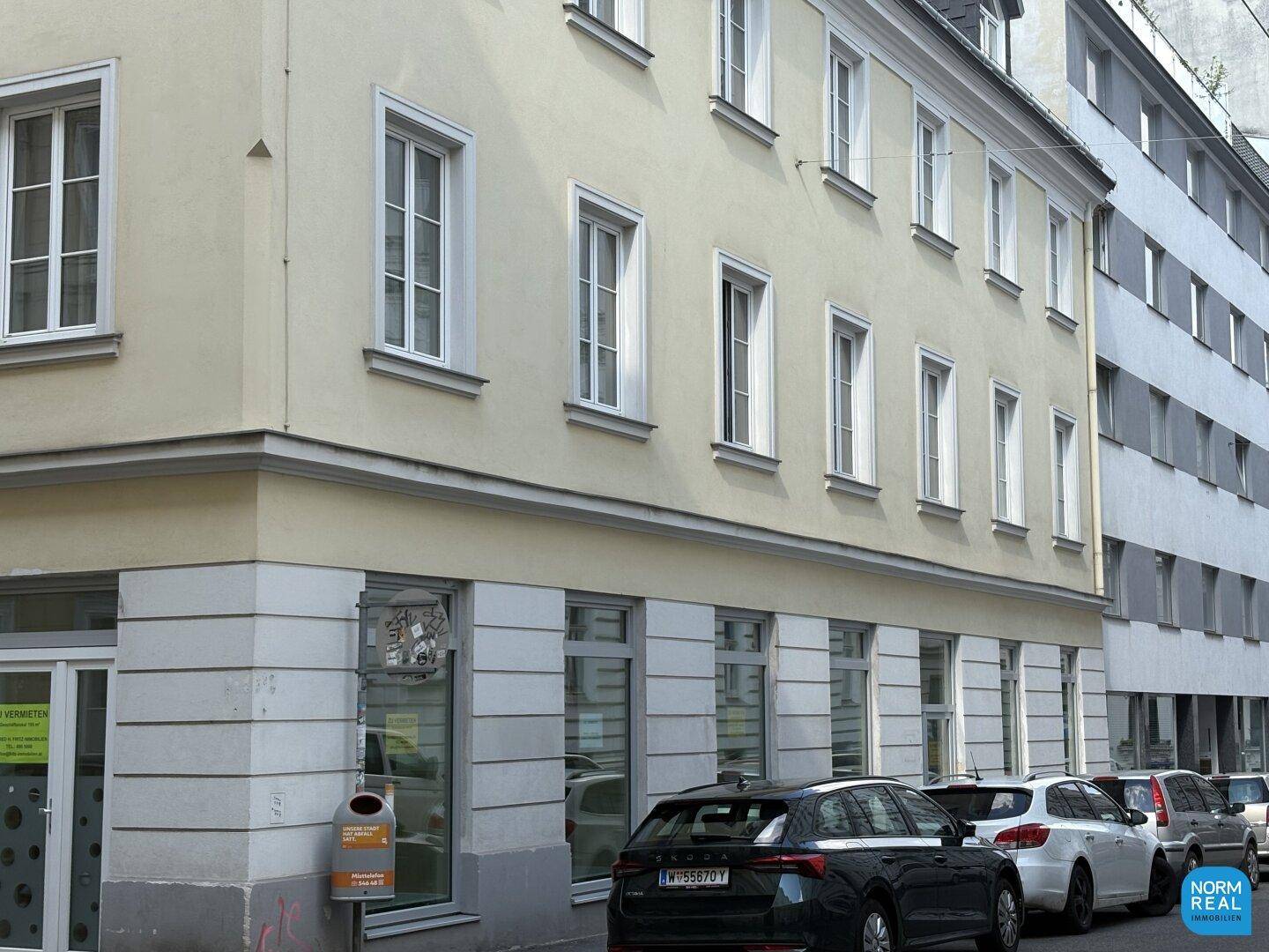 Historische Gebäudefassade mit vielen Fenstern und Geschäften im Erdgeschoss an einer Straße.