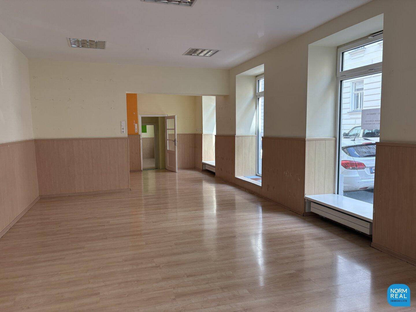 Geräumiger Gewerberaum mit Holzpaneelen an den Wänden und großen Fenstern zur Straße.