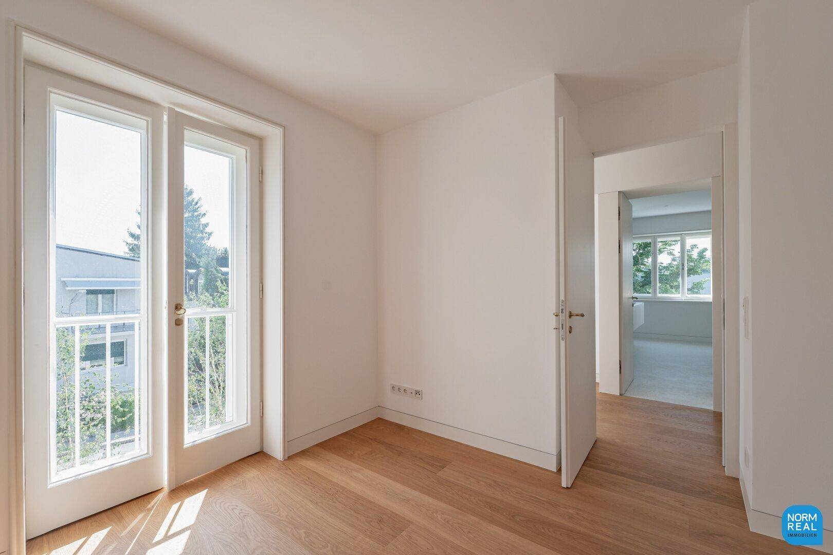 Leeres Zimmer mit hellem Parkettboden und französischen Balkontüren, die viel Licht hereinlassen.