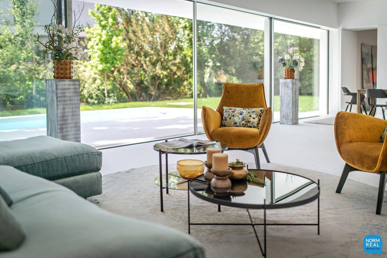 Helles Wohnzimmer mit raumhohen Fenstern, modernem Mobiliar und Blick auf den Pool und Garten.