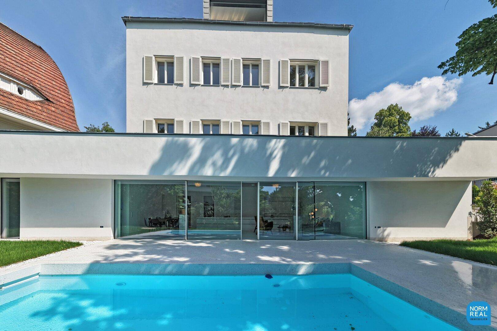 Ansicht des Gebäudes vom Pool aus, mit großer Glasfassade und weißer Architektur.