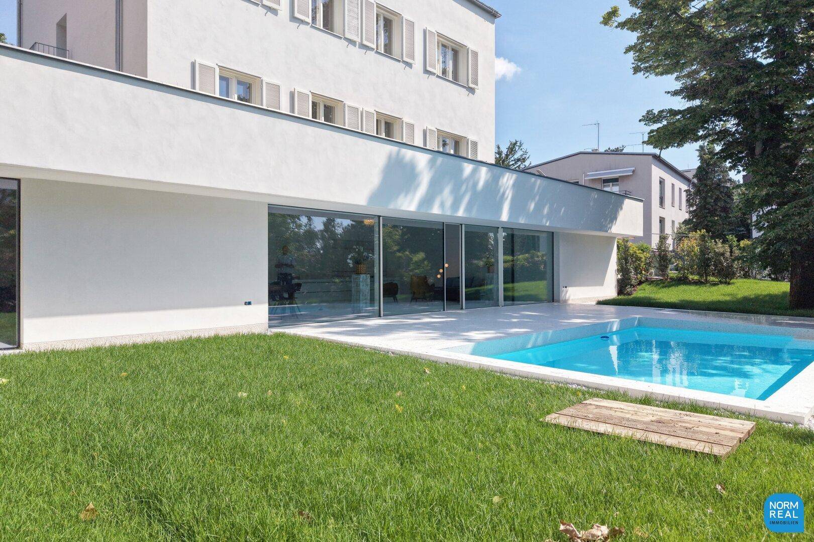Außenbereich mit Rasenfläche, modernem Pool und der Glasfassade des Gebäudes.