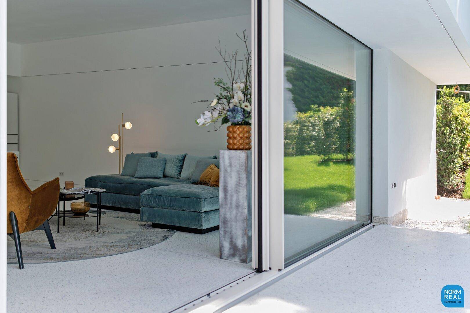 Blick vom Außenbereich in das helle Wohnzimmer durch große Glasschiebetüren mit Gartenblick.