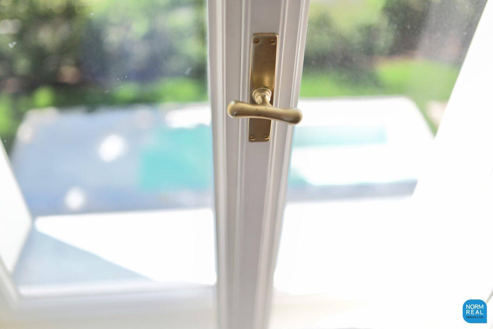 Detailaufnahme eines Fenstergriffs mit Blick auf den Außenpoolbereich.