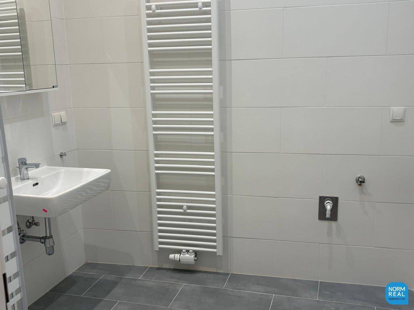 Helles Badezimmer mit Einzelwaschbecken, beheiztem Handtuchhalter und Anschluss für Waschmaschine, sehr funktional.