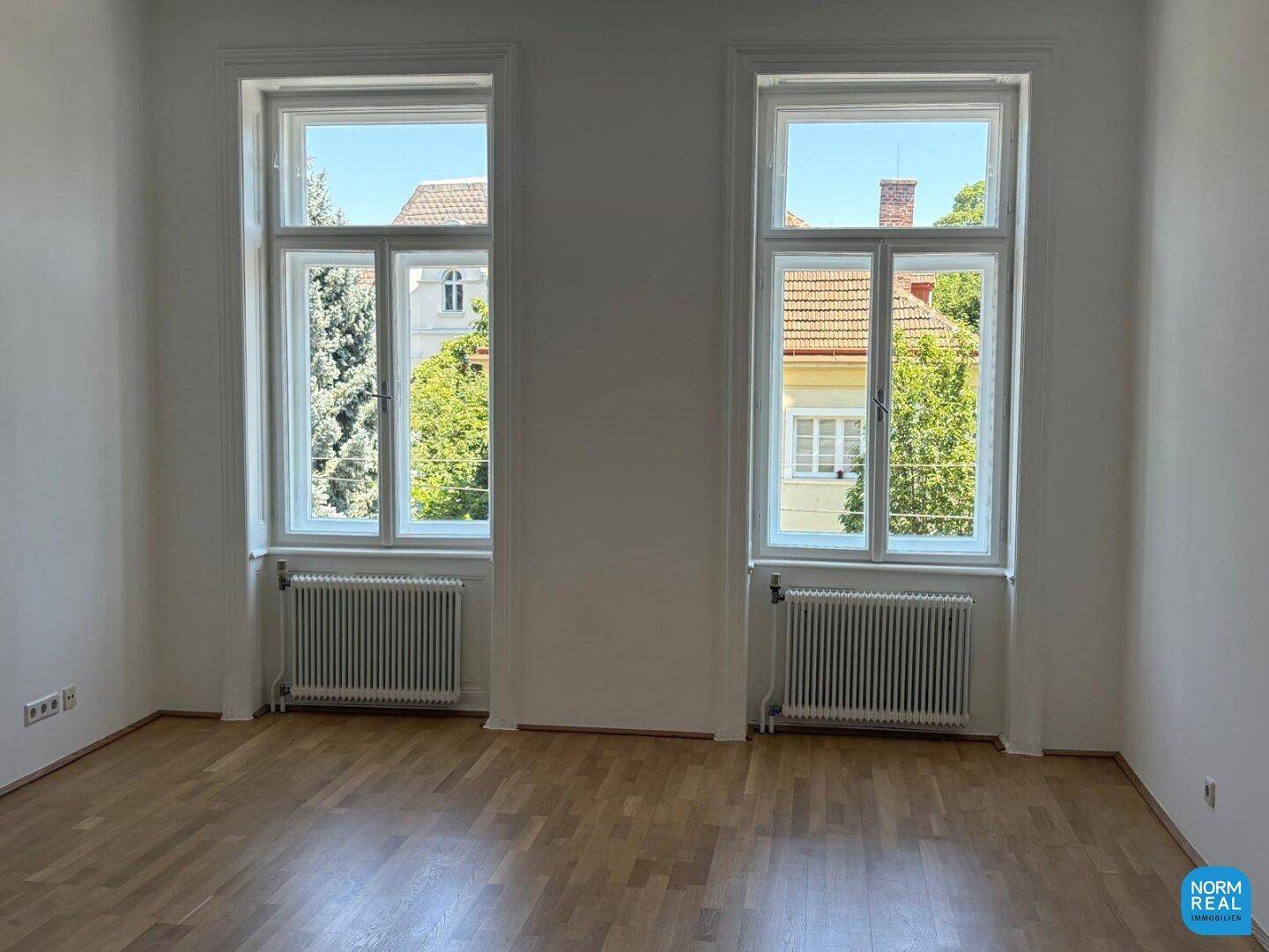Geräumiger, heller Raum mit Parkettboden und zwei großen Fenstern, die viel Licht spenden und eine offene Atmosphäre schaffen.