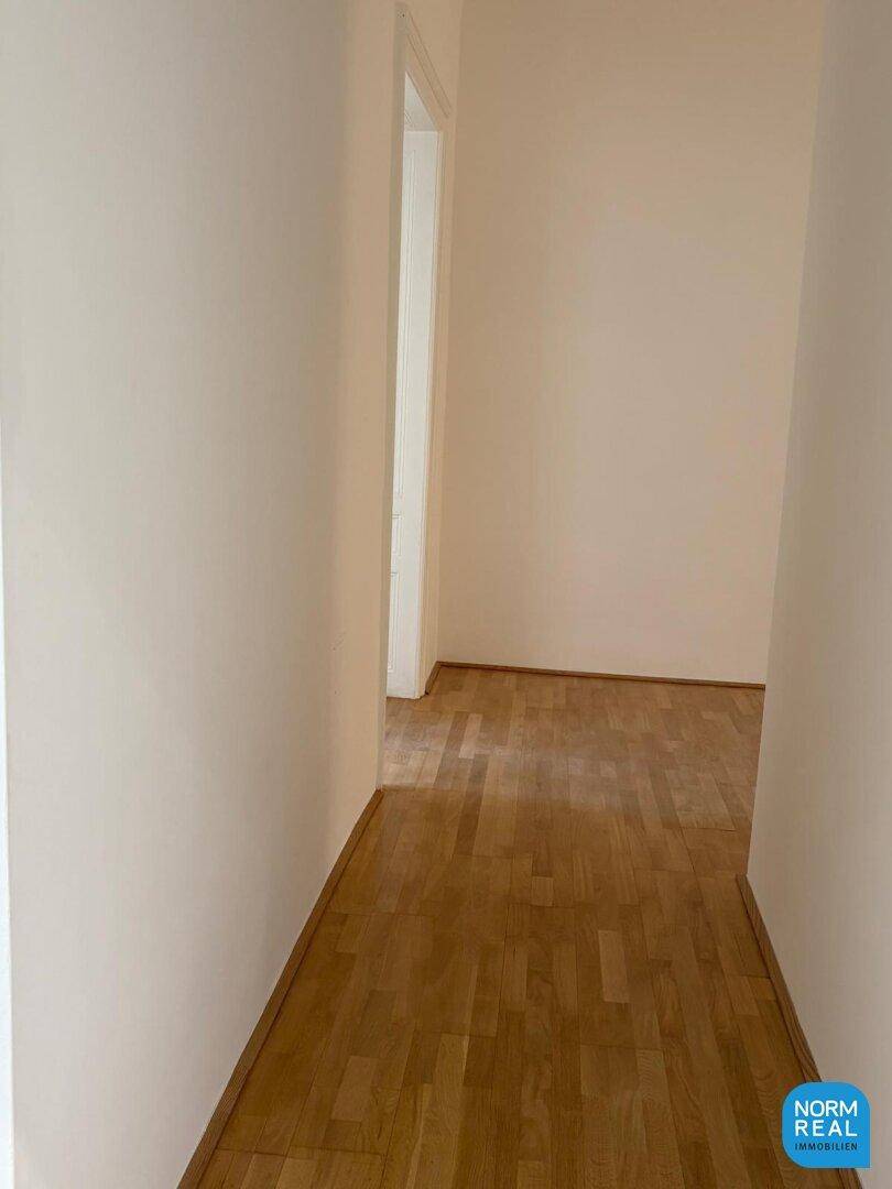 Langer, heller Flur mit Parkettboden, der verschiedene Räume miteinander verbindet und einladend wirkt.