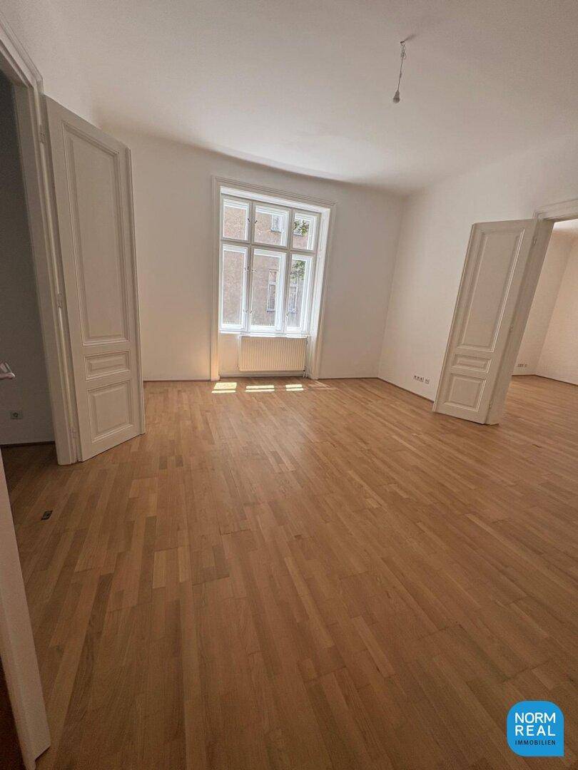 Geräumiger, heller Raum mit Parkettboden und großem Fenster, das viel Tageslicht hereinlässt und eine angenehme Atmosphäre schafft.