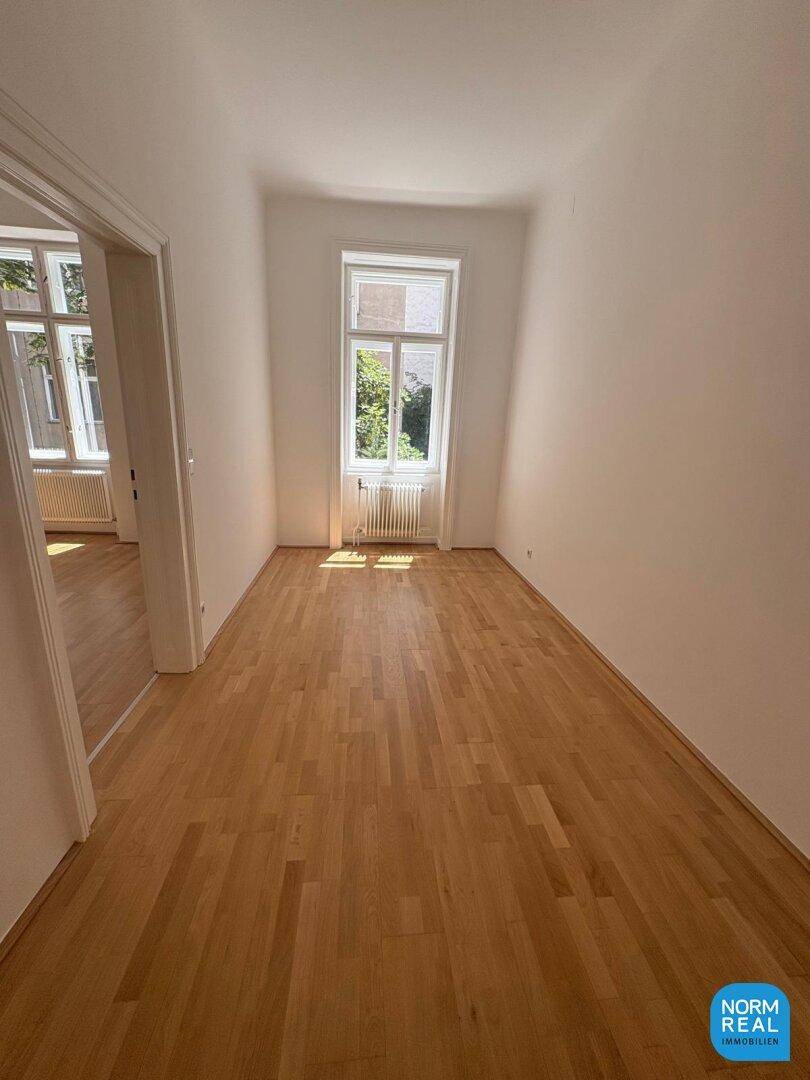Langer, heller Raum mit Parkettboden und einem Fenster, das den Blick ins Grüne freigibt und Ruhe verspricht.