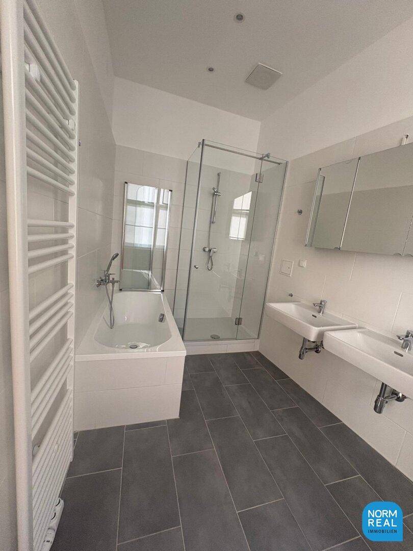 Großes, modernes Badezimmer mit Badewanne, Duschkabine, Doppelwaschbecken und Spiegelschrank auf Fliesenboden.