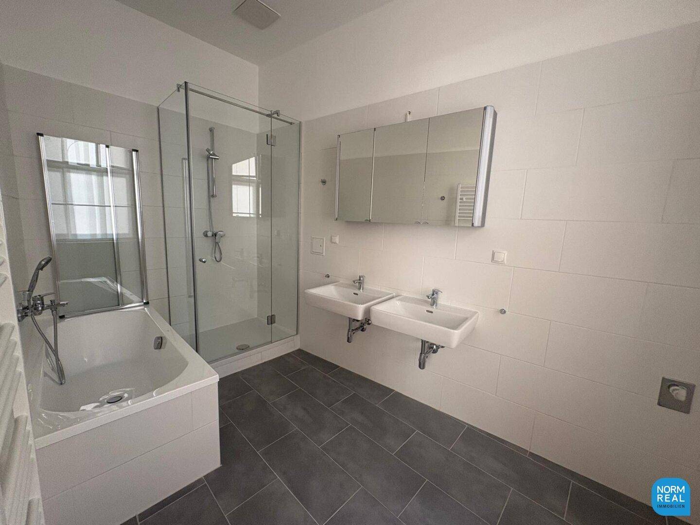 Großes, modernes Badezimmer mit Badewanne, Duschkabine, Doppelwaschbecken und Spiegelschrank auf Fliesenboden.