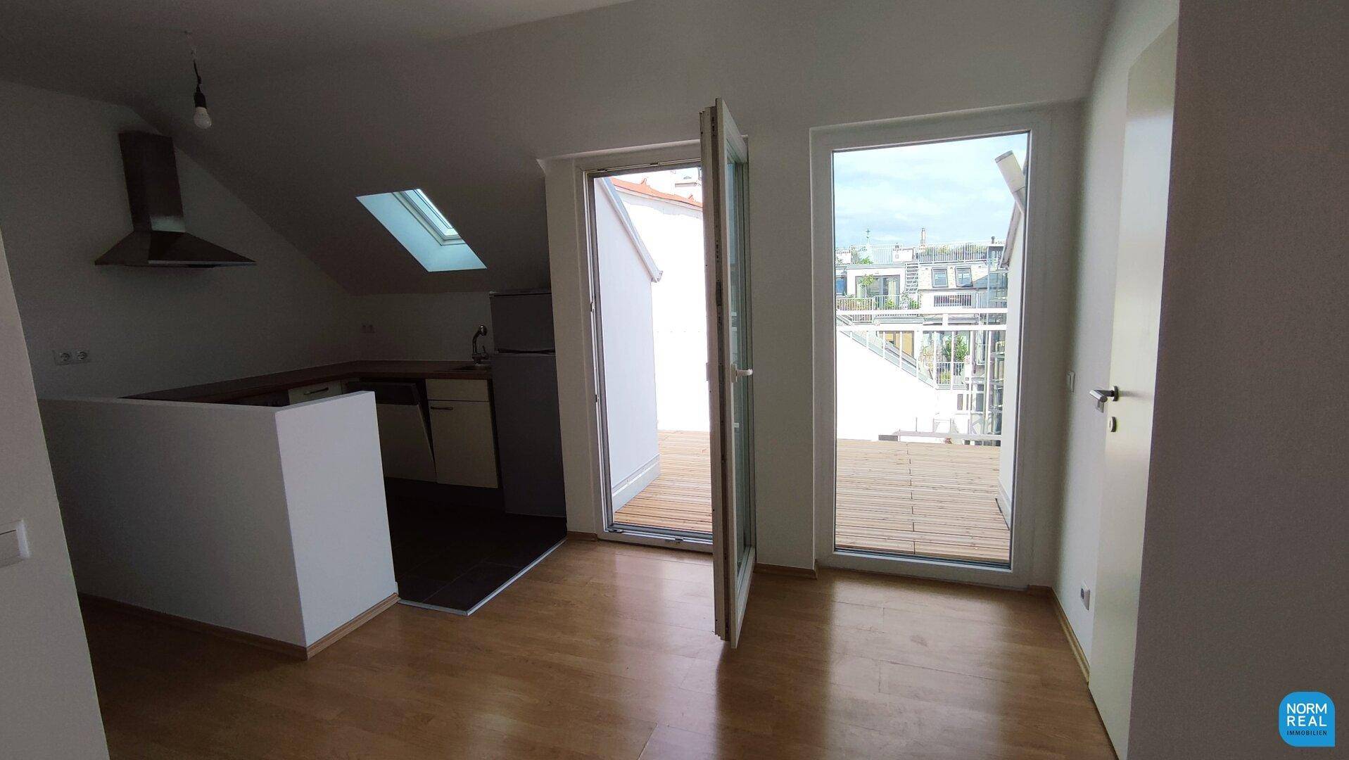 Heller Wohnbereich mit Holzboden, Dachschrägen und Zugang zur Dachterrasse.