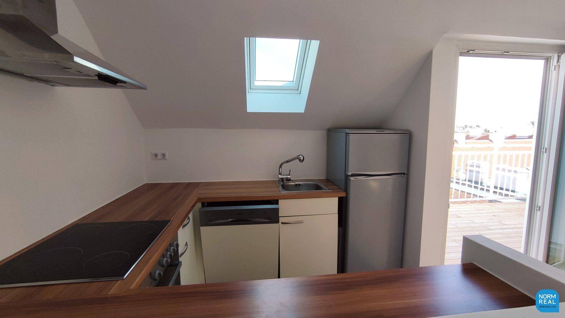 Küchenzeile mit Holzarbeitsplatte, Spüle und Kühlschrank unter einem Dachfenster.