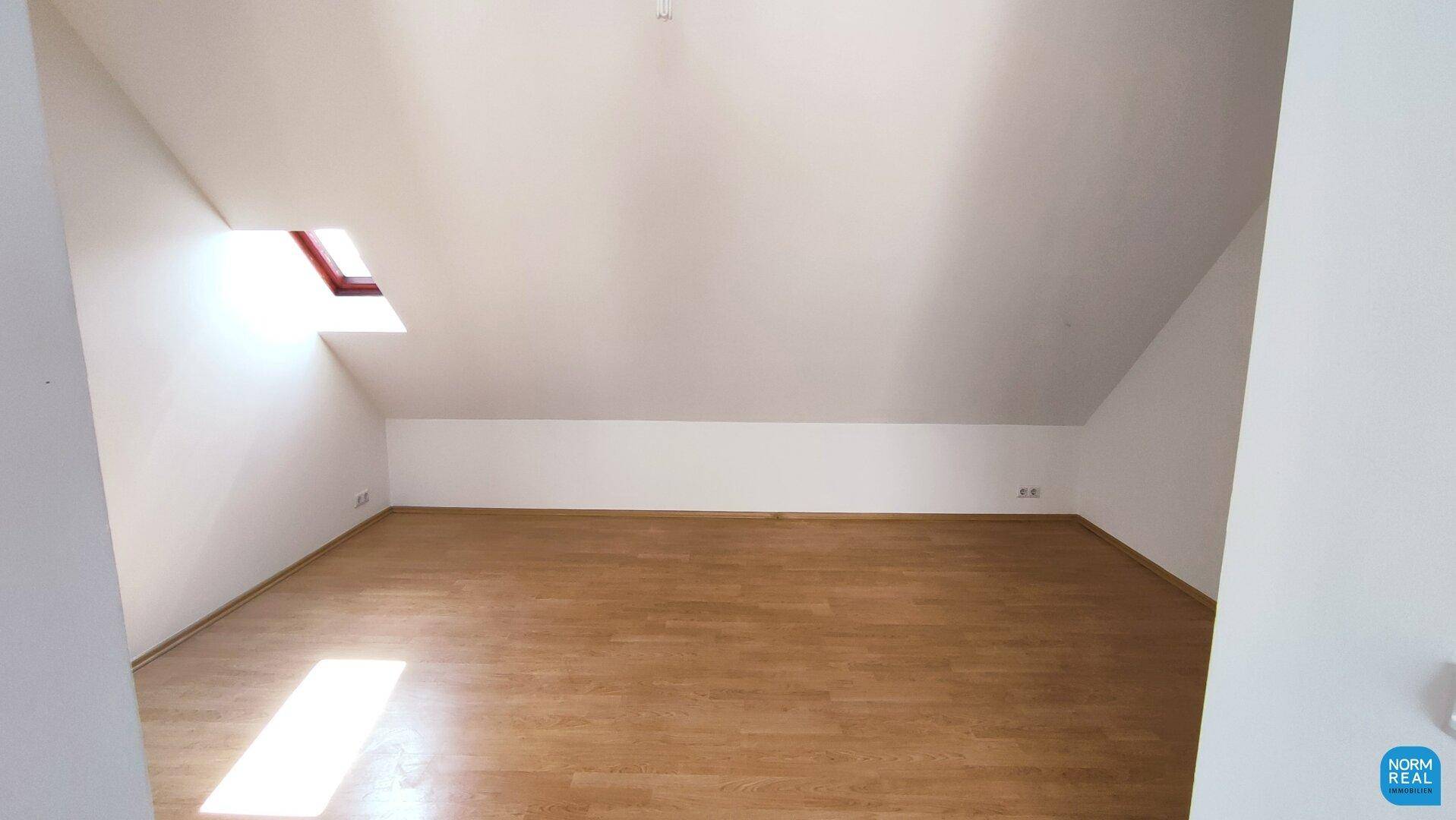 Geräumiger, heller Raum mit Holzboden und Dachschräge, ideal als Wohn- oder Schlafzimmer.