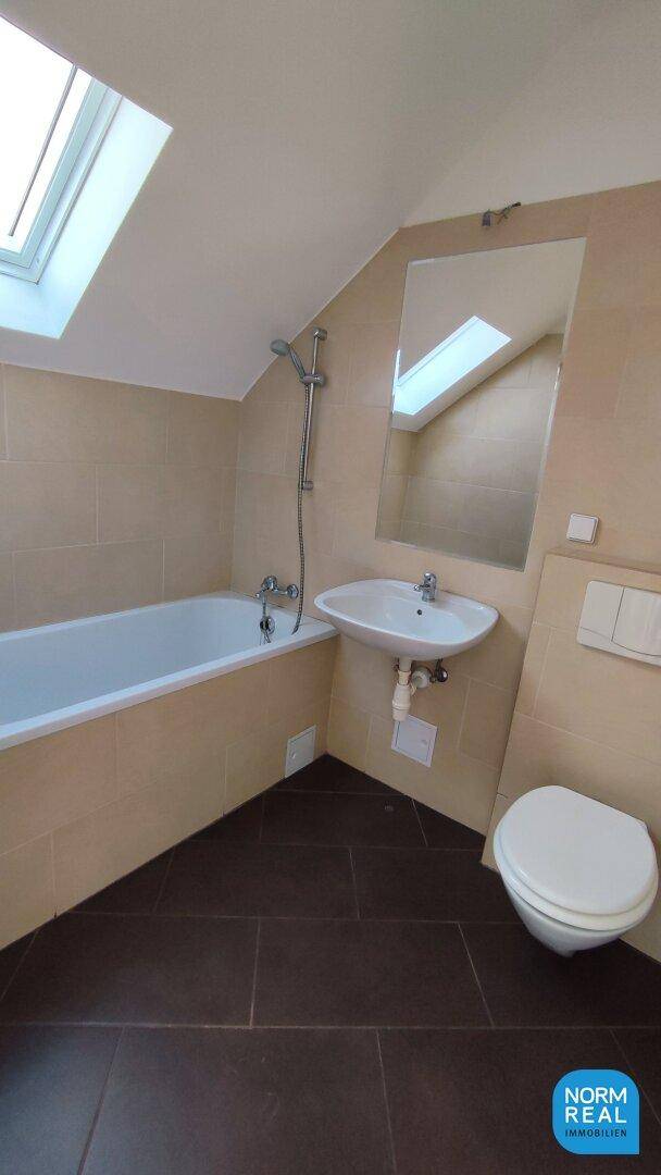 Badezimmer mit Badewanne, Waschbecken, Toilette und Dachfenster unter der Dachschräge.