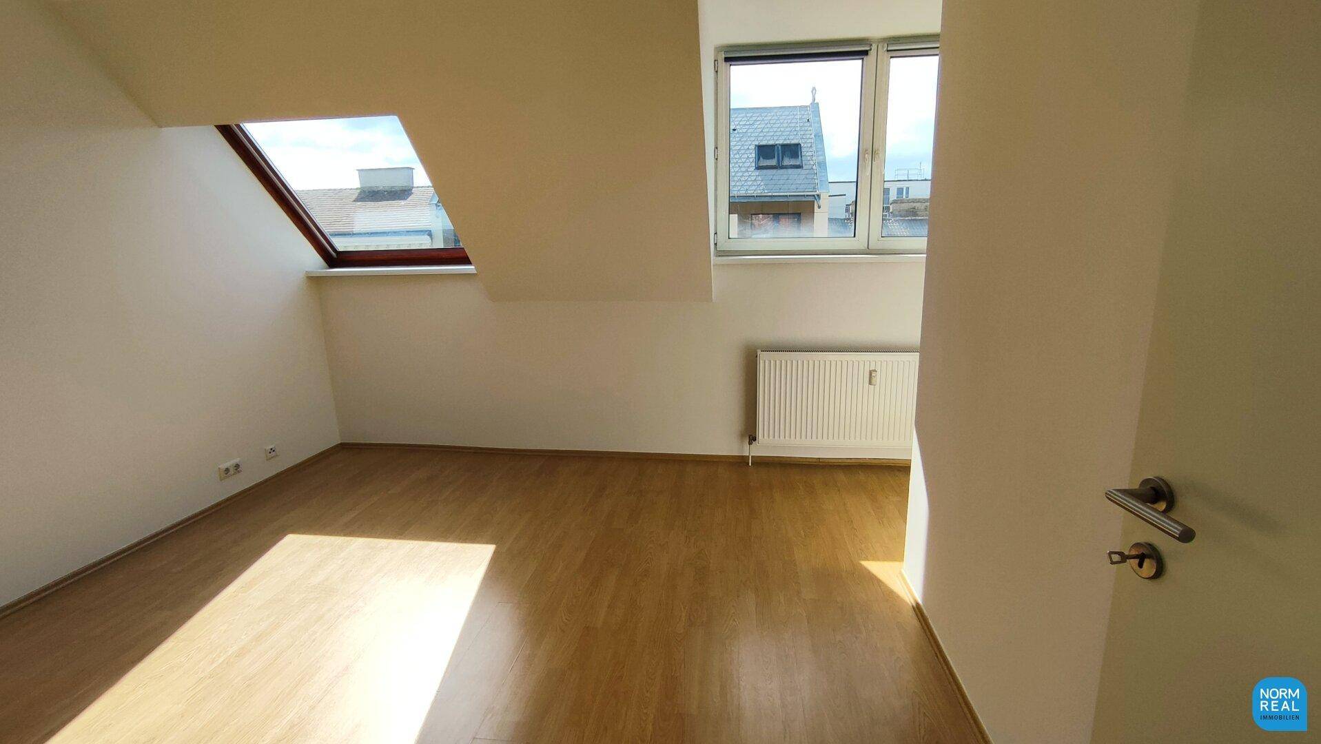 Heller Raum mit Holzboden, Dachfenster und normalem Fenster, geeignet als Schlafzimmer.