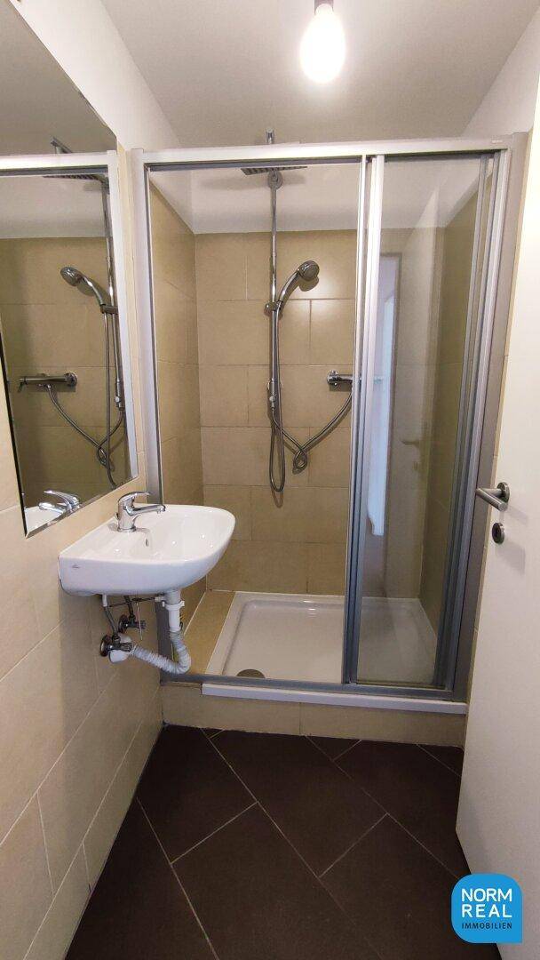 Modernes Badezimmer mit Duschkabine, Waschbecken und Fliesenboden in neutralen Farben.