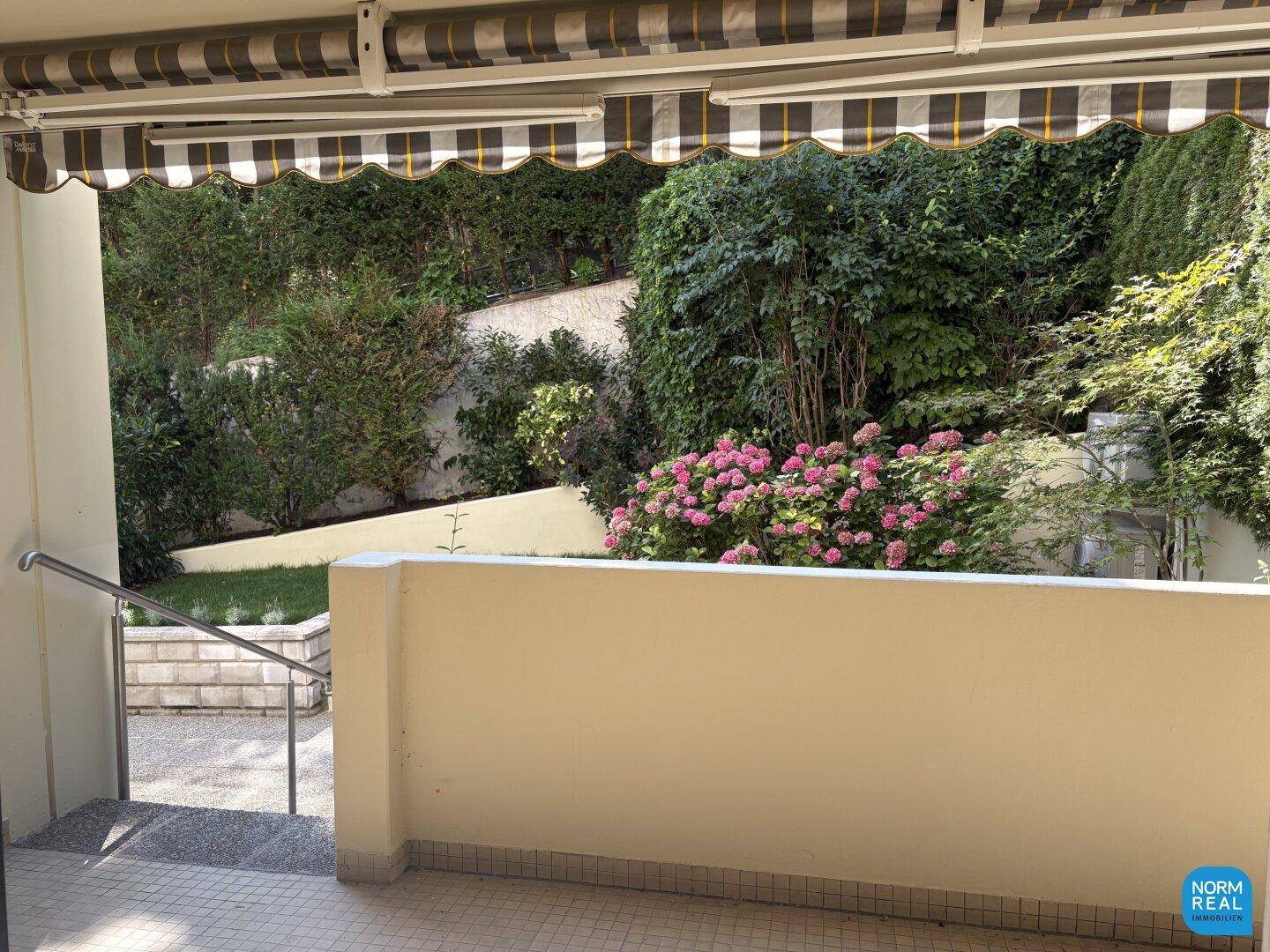 Überdachte Terrasse mit Markise und Blick auf den grünen Gartenbereich.