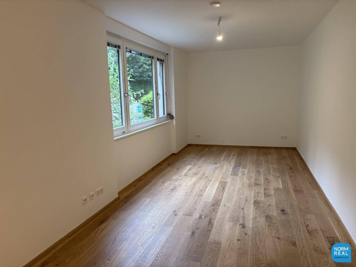 Ruhiges Zimmer mit Holzboden und Fensterblick ins Grüne, ideal als Schlaf- oder Arbeitszimmer.