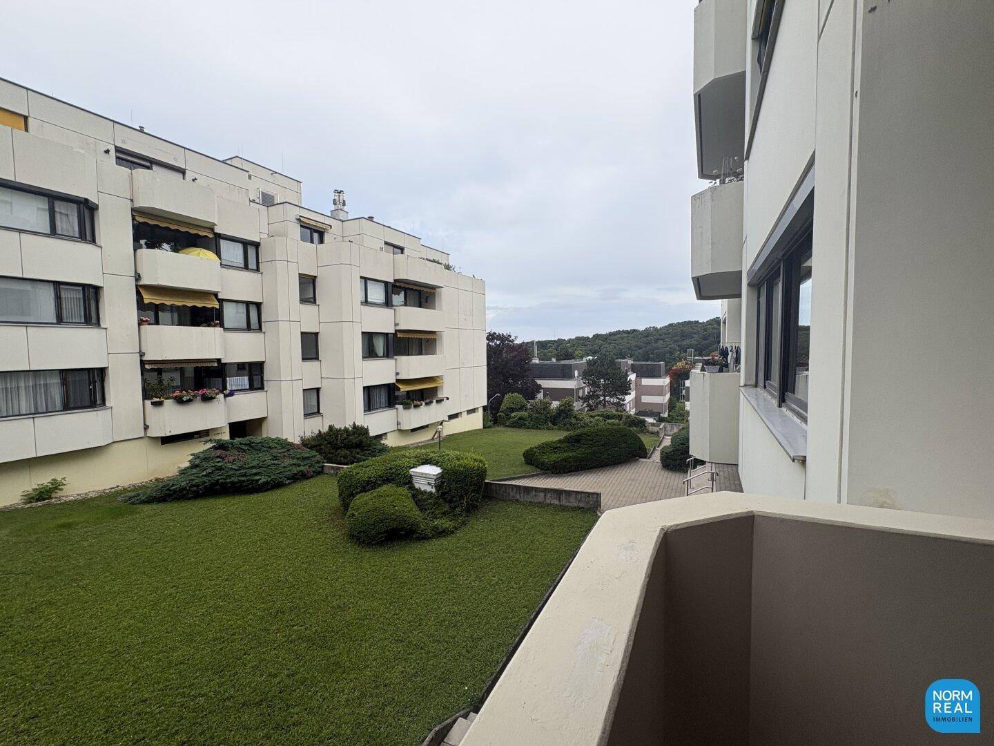 Blick vom Balkon auf eine gepflegte Grünanlage und umliegende Wohngebäude.