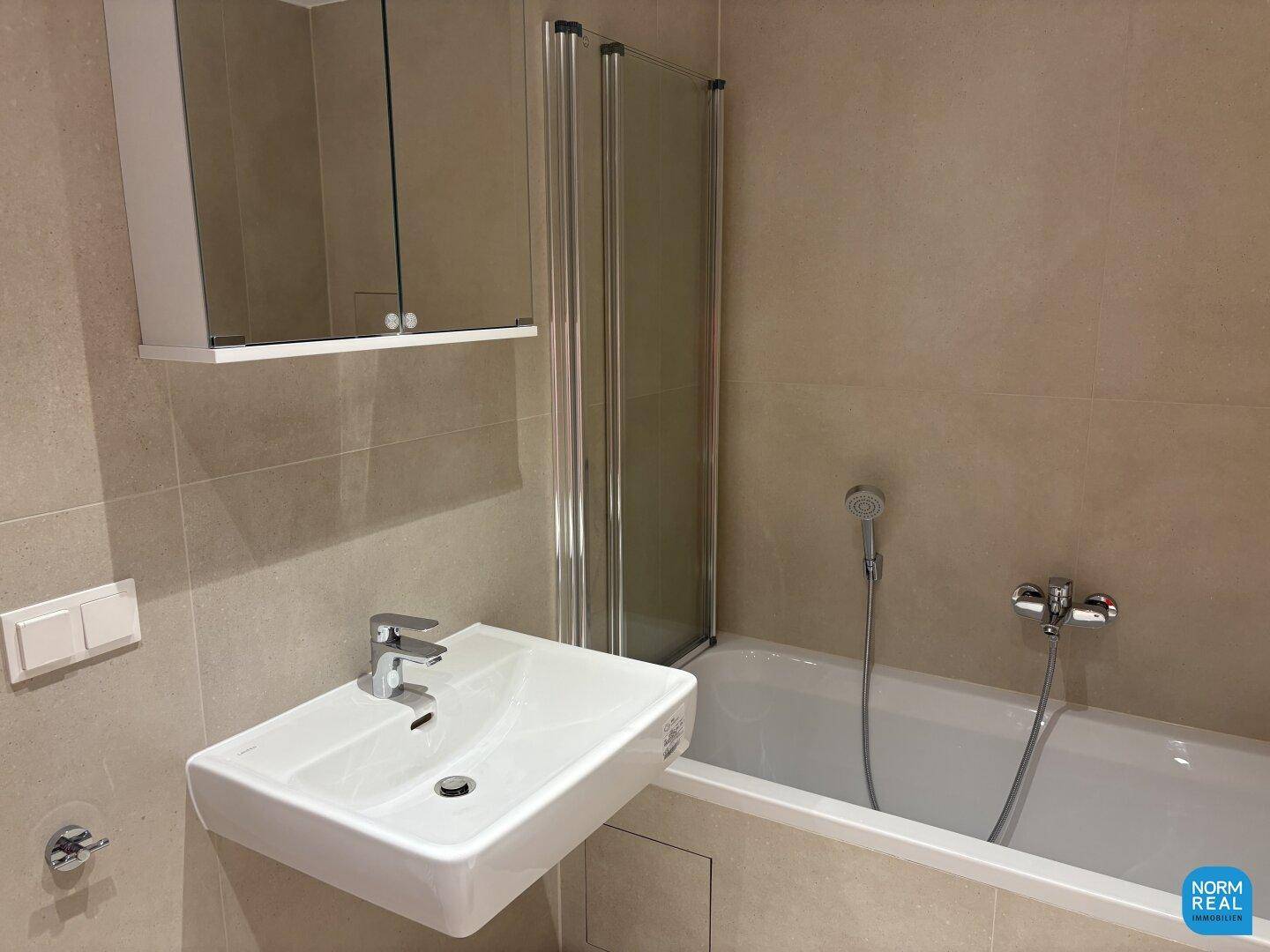Modernes Badezimmer mit Badewanne, Waschbecken und Spiegelschrank, in hellen Fliesen gehalten.