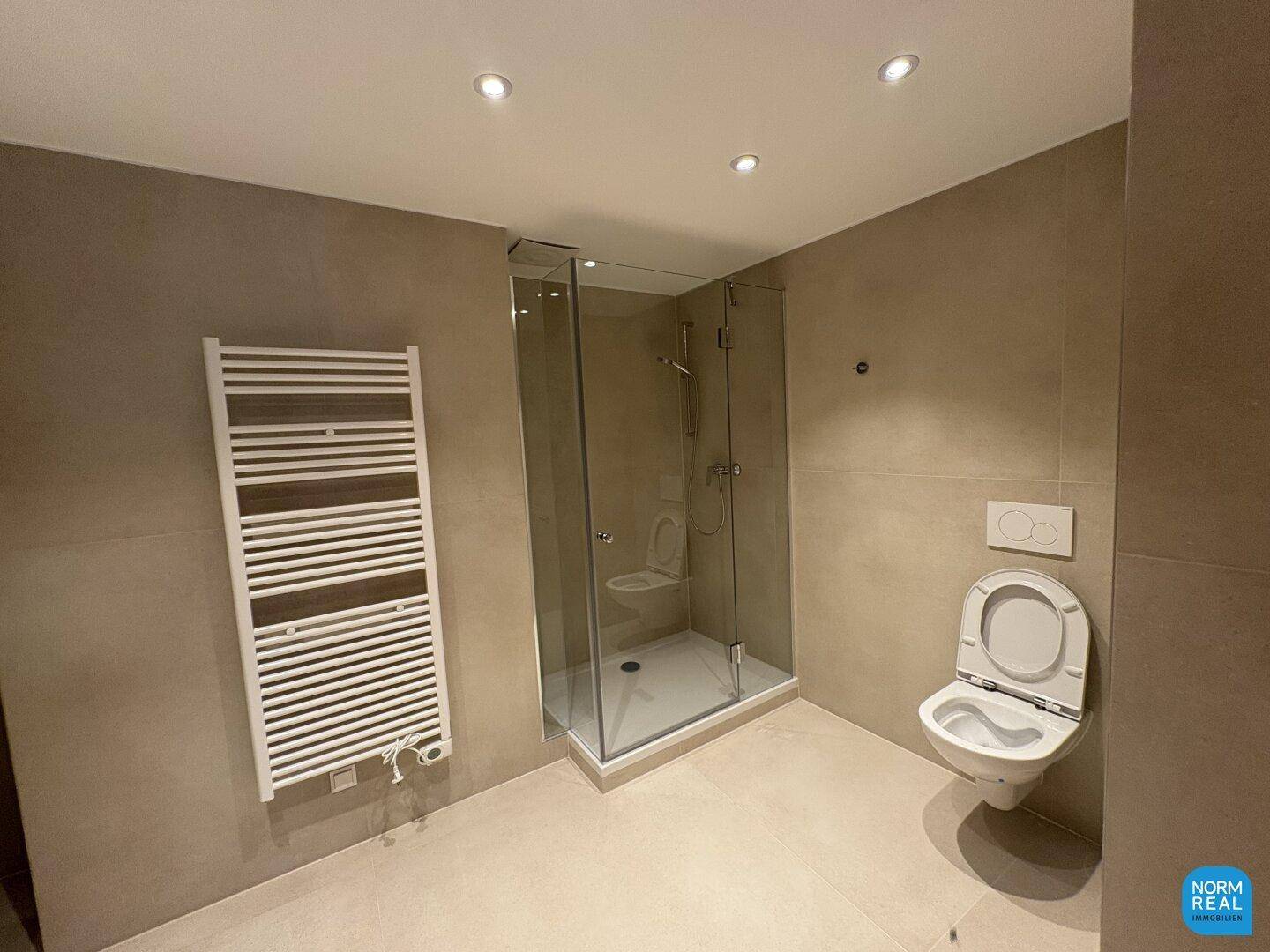 Modernes Badezimmer mit ebenerdiger Dusche, wandhängendem WC und beheiztem Handtuchhalter.