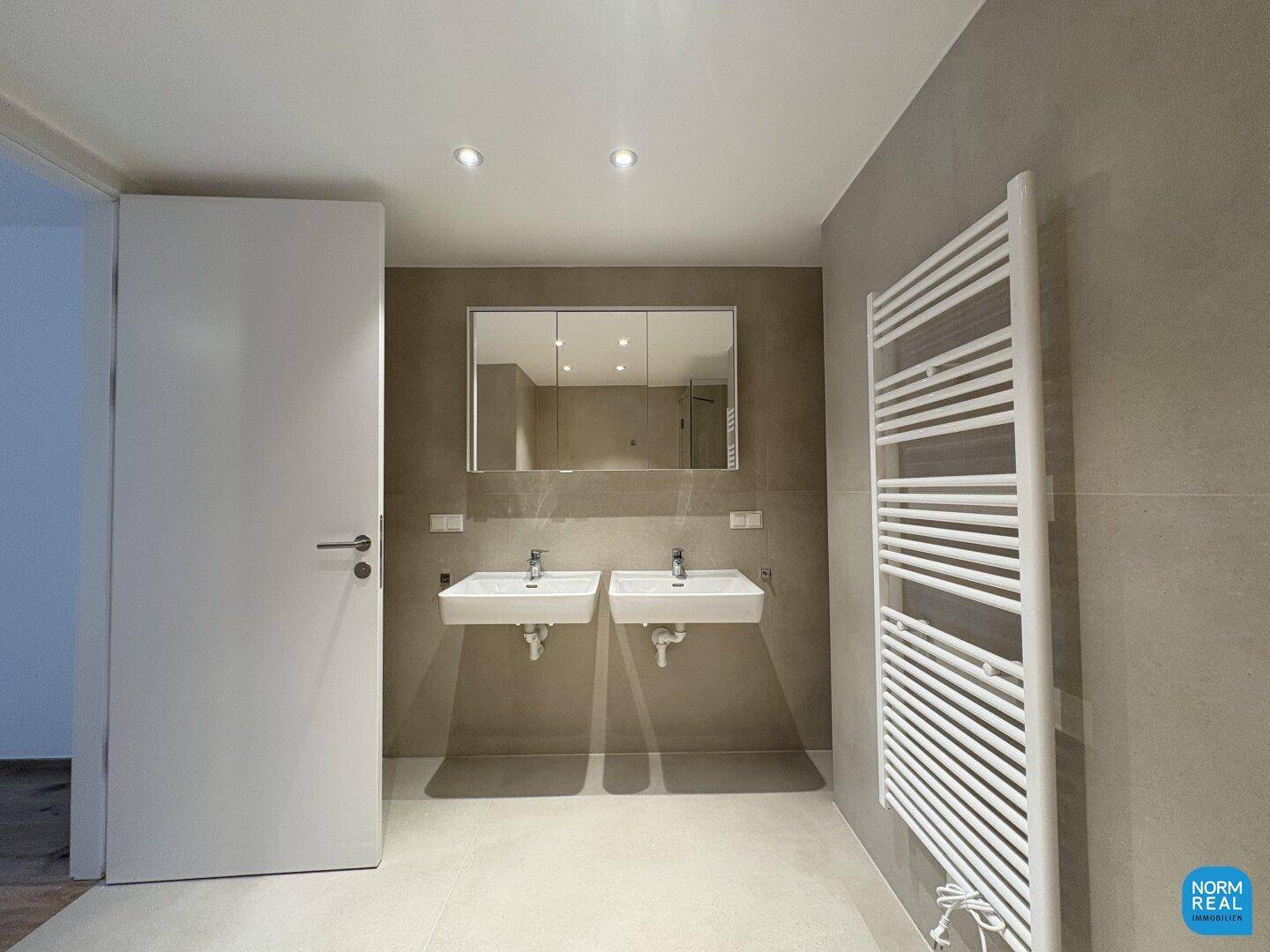 Geräumiges Badezimmer mit Doppelwaschbecken, großem Spiegelschrank und beheiztem Handtuchhalter.