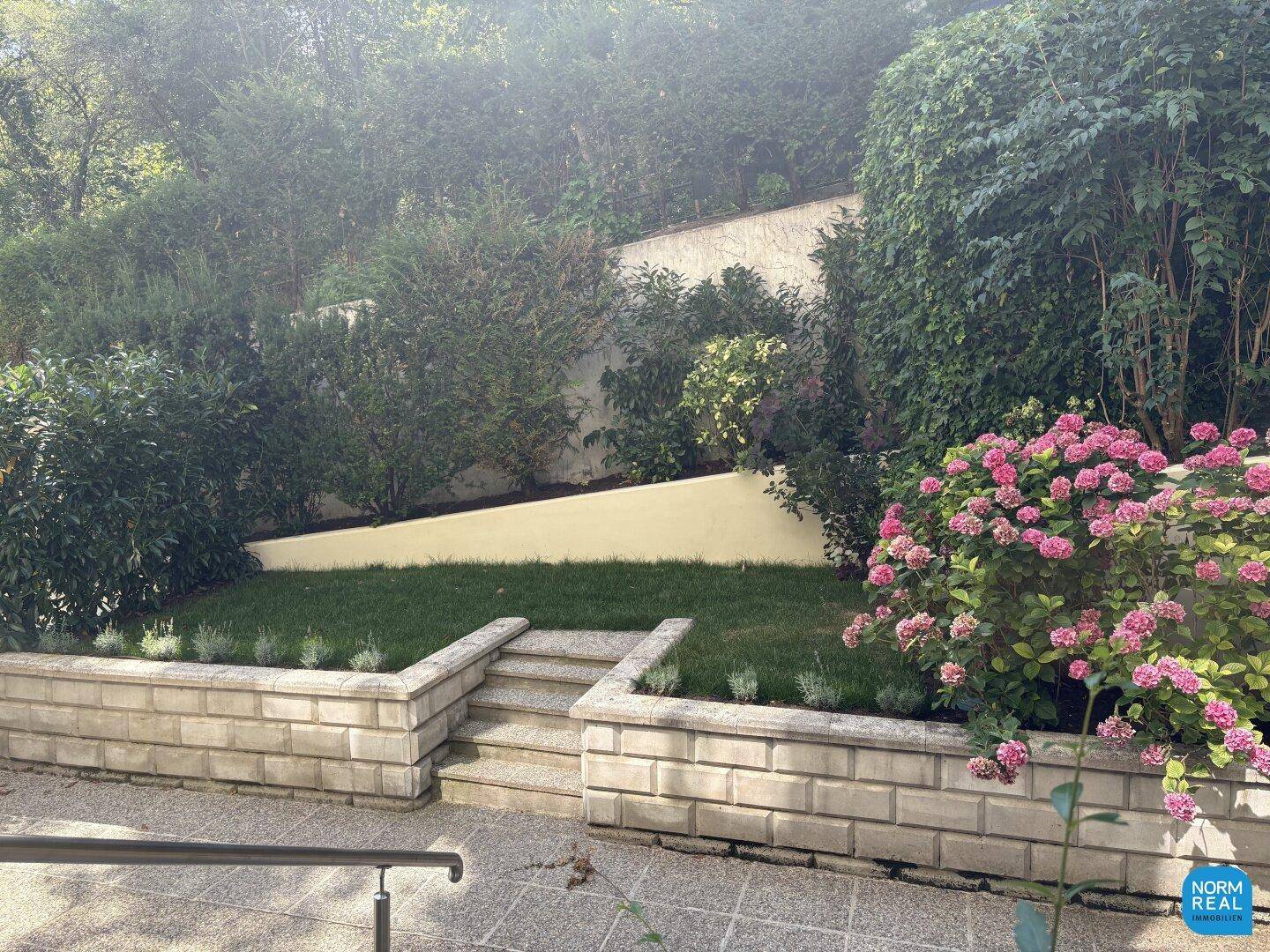 Gestufter Gartenbereich mit Rasen, Blumenbeeten und hohen Hecken für Privatsphäre.