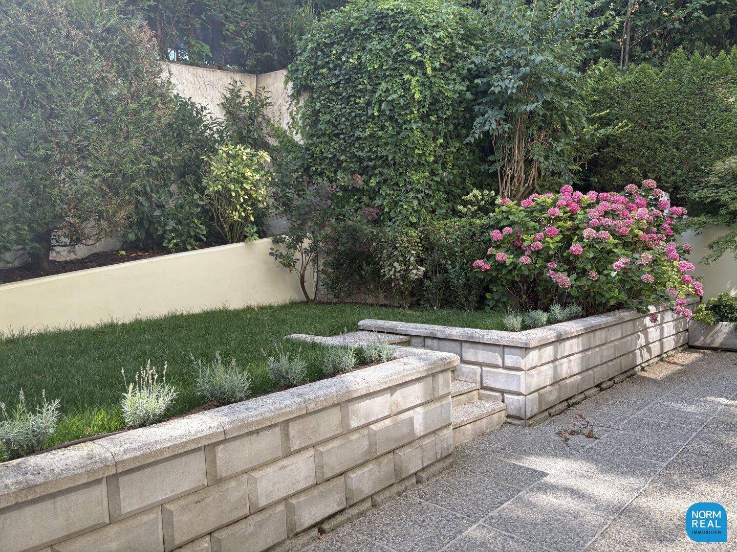 Gepflegter Gartenbereich mit Rasenflächen, Blumenbeeten und Natursteinmauern.