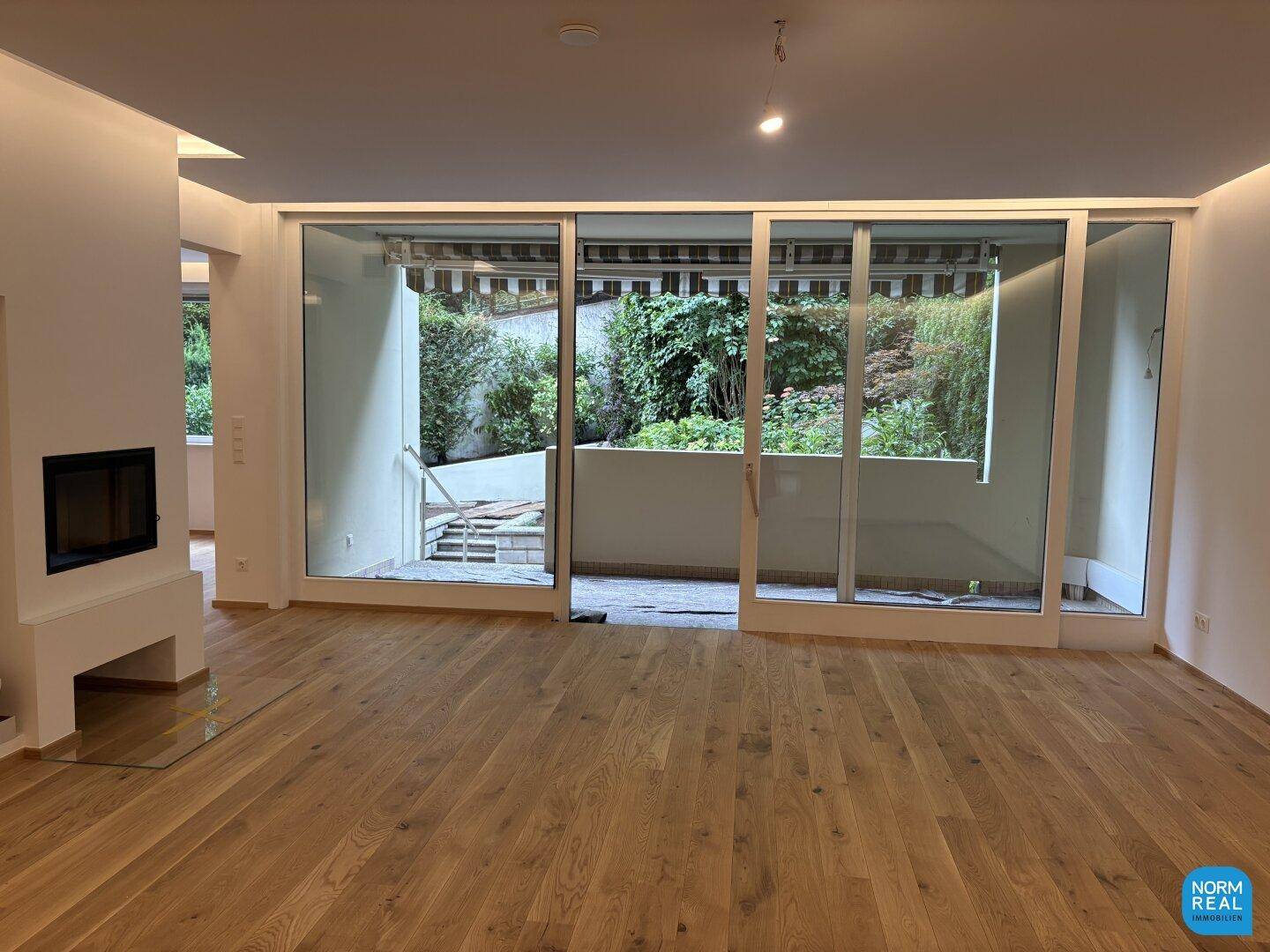 Helles Wohnzimmer mit Holzboden, modernem Kamin und Zugang zu einer Außenterrasse.