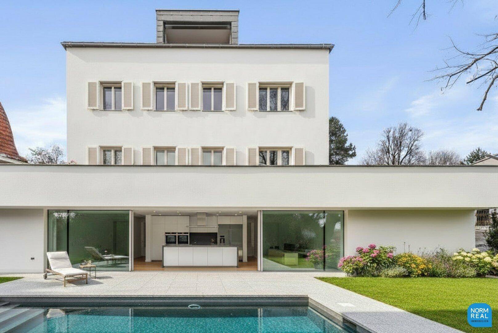 Moderne Einbauküche sichtbar durch die Glasfront, mit Poolbereich im Vordergrund.