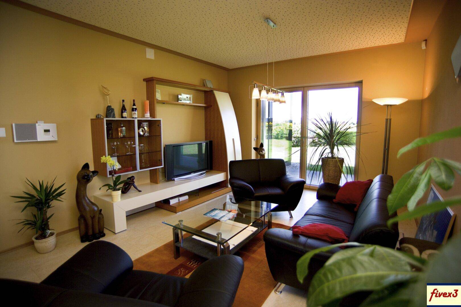 Gemütliches Wohnzimmer mit dunklen Ledersofas, TV-Möbeln und Zugang zum Garten.
