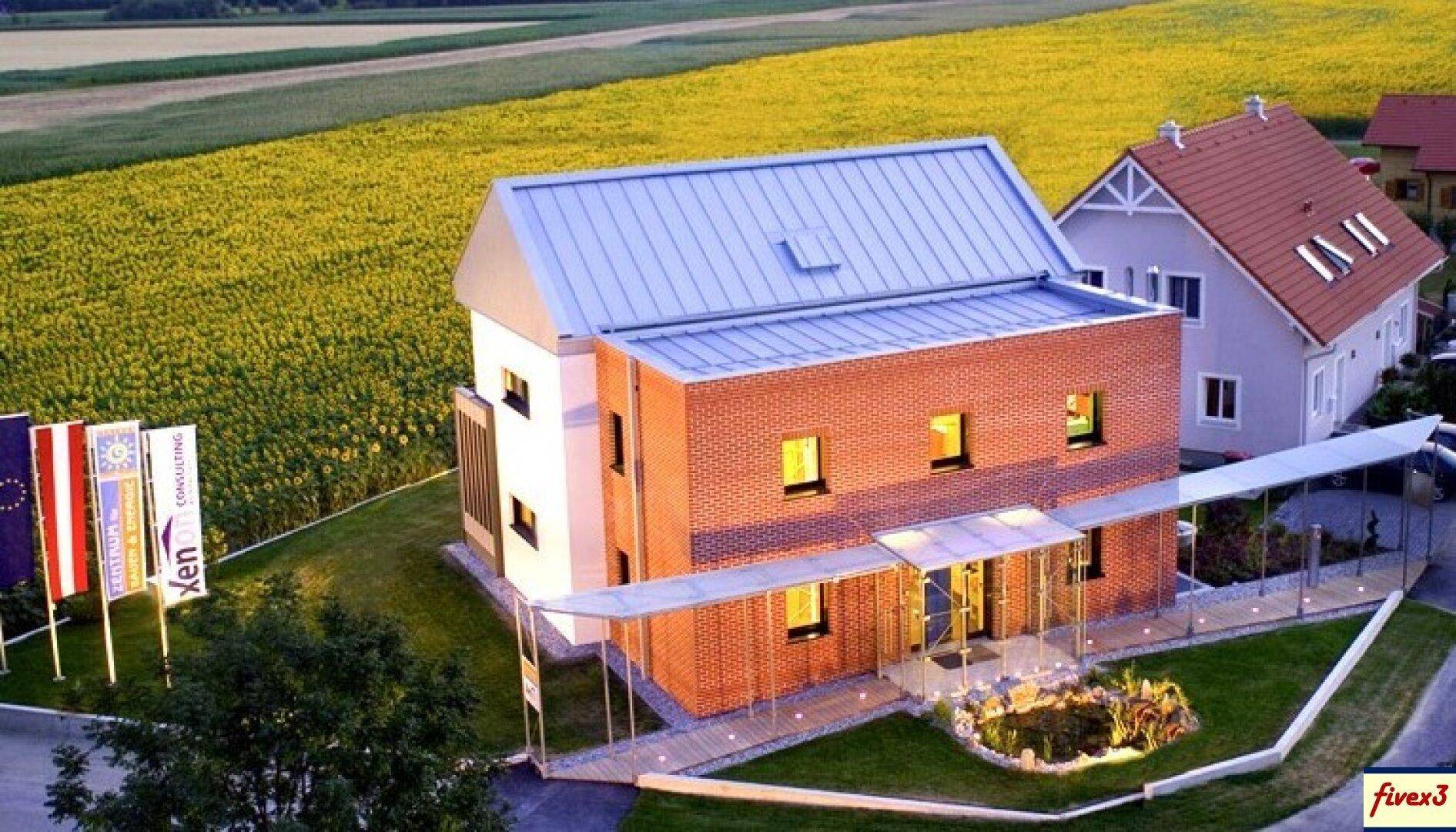 Luftaufnahme eines modernen Backsteinhauses mit Solaranlage und Carport, umgeben von Feldern.