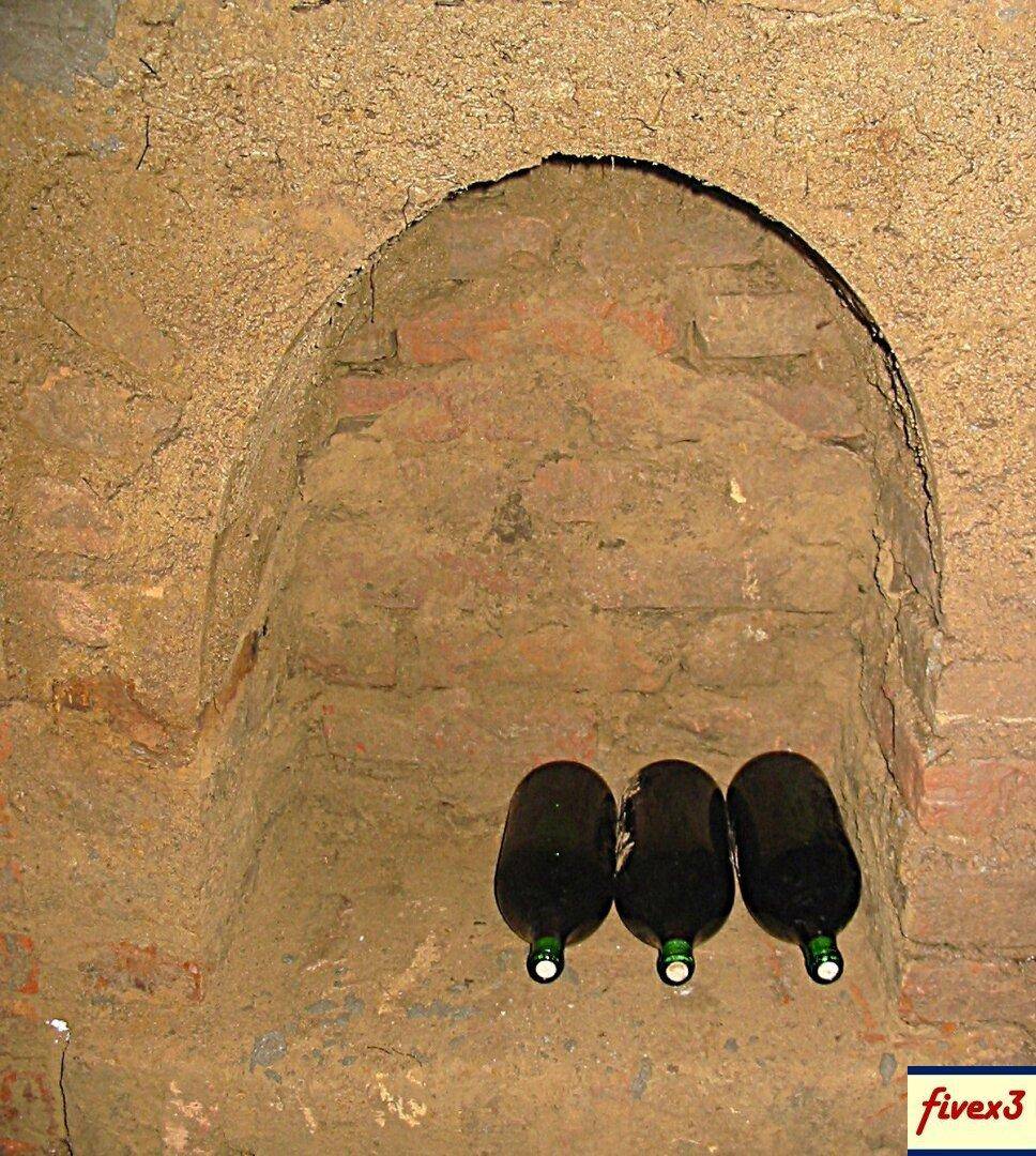 Nahaufnahme einer gewölbten Nische in einer Ziegelwand, in der drei Weinflaschen traditionell gelagert werden.
