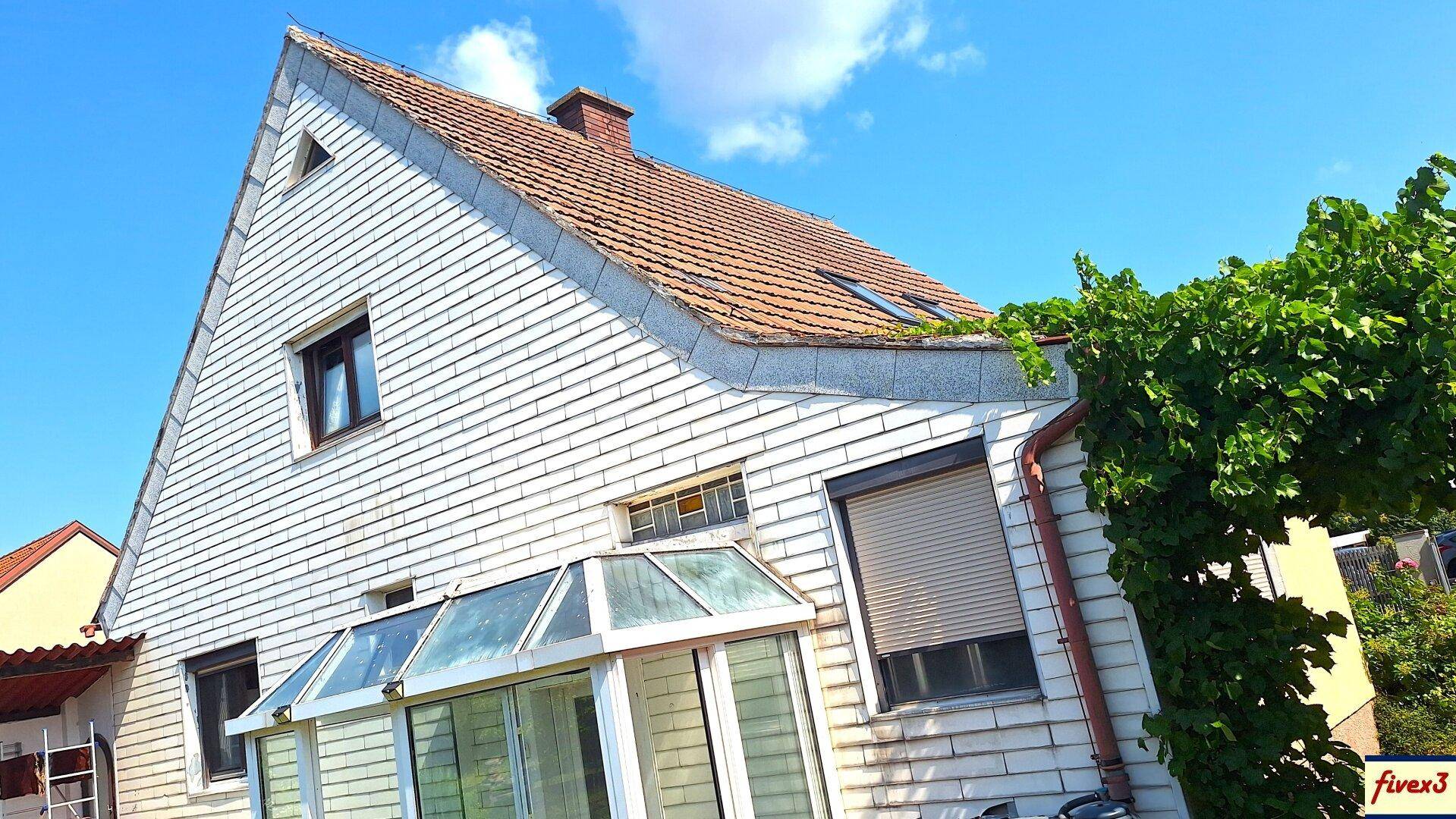 Seitenansicht des Hauses mit Wintergarten, Dachfenstern und weißer Fassadenverkleidung.