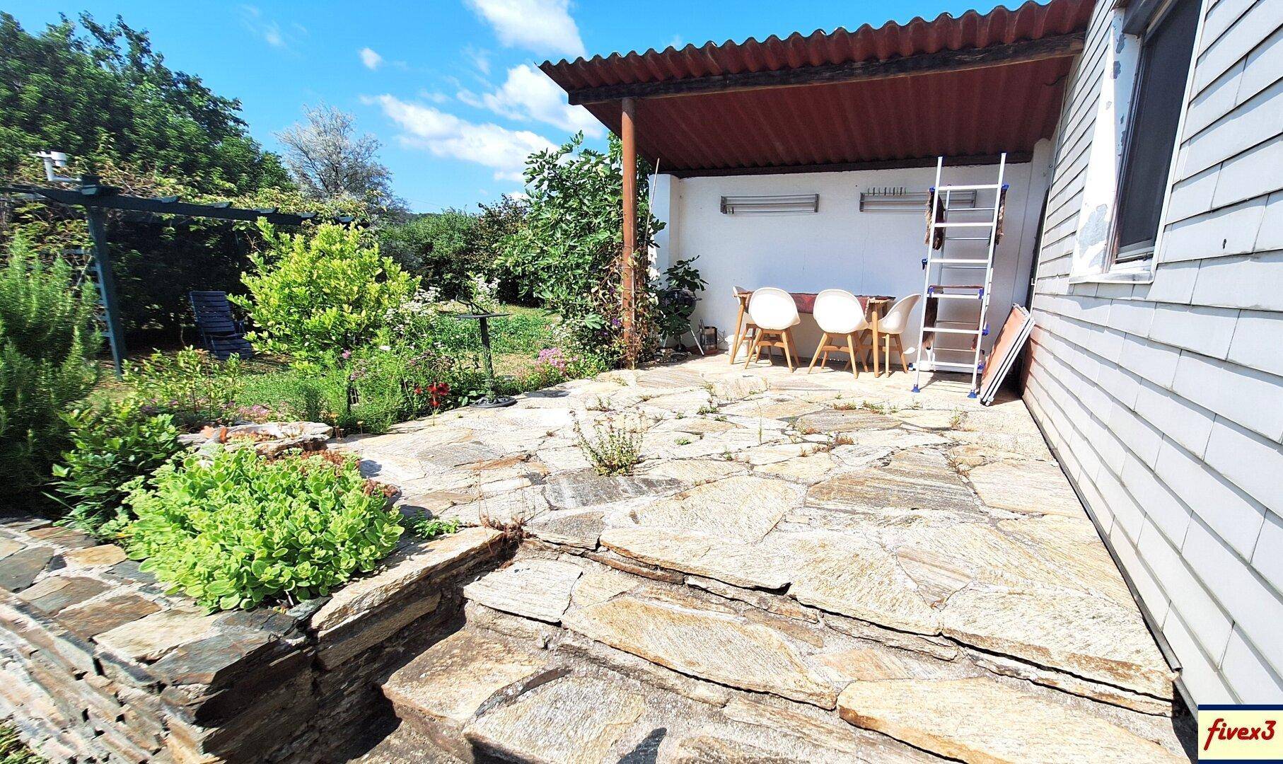 Überdachte Steinterrasse mit Sitzgelegenheiten und Blick in den grünen Garten.