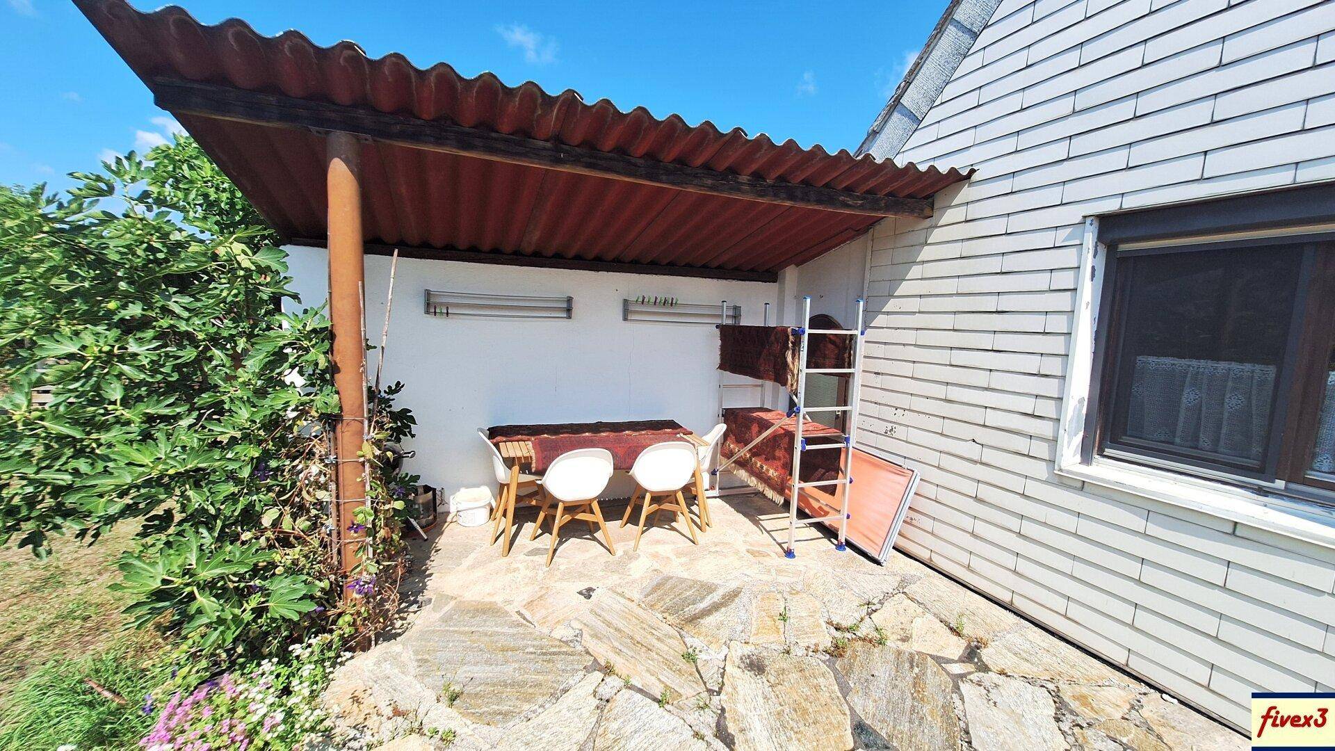 Gemütliche überdachte Terrasse mit Esstisch und Stühlen, umgeben von Pflanzen.
