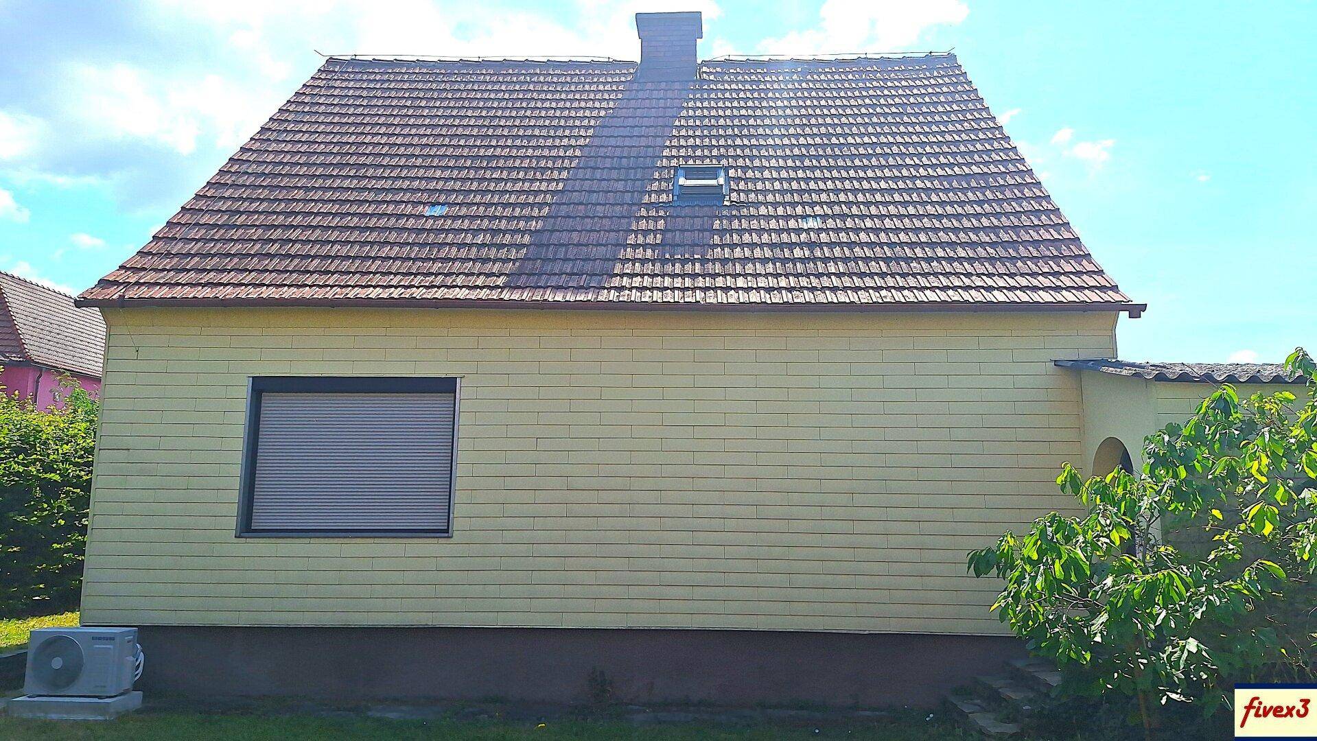 Seitenansicht des Hauses mit gelber Fassade, Satteldach und einem Fenster mit Rollladen.