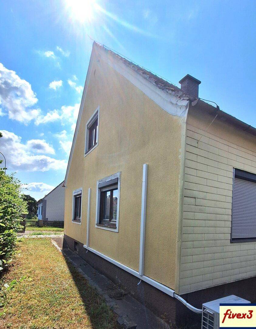 Seitenansicht des Hauses mit gelber und weißer Fassade unter strahlendem Sonnenschein.