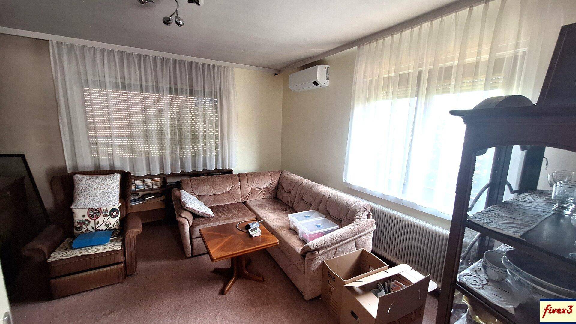 Gemütliches Wohnzimmer mit Sofa, Teppichboden und Fenstern mit Vorhängen.
