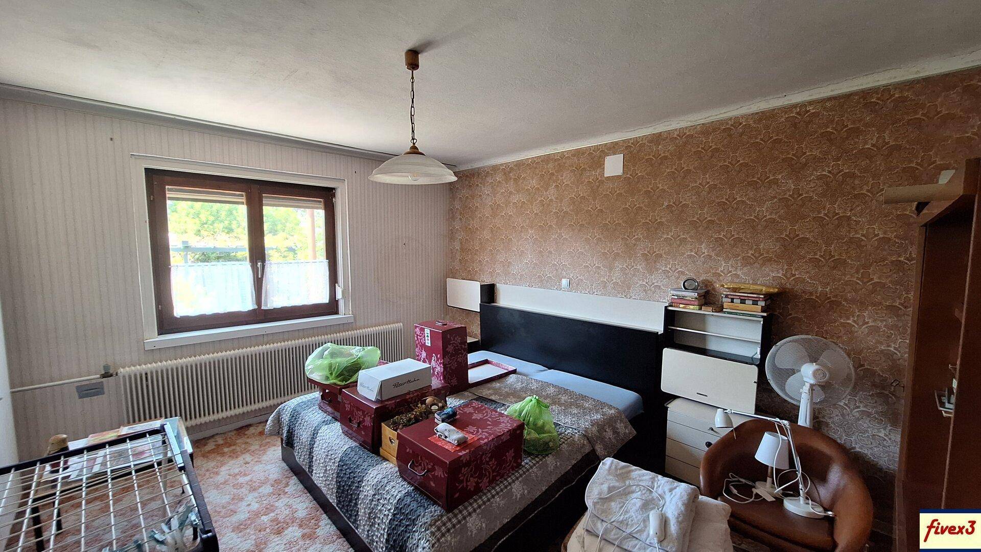 Schlafzimmer mit Doppelbett, gemusterter Tapete und Fenster mit Blick ins Grüne.