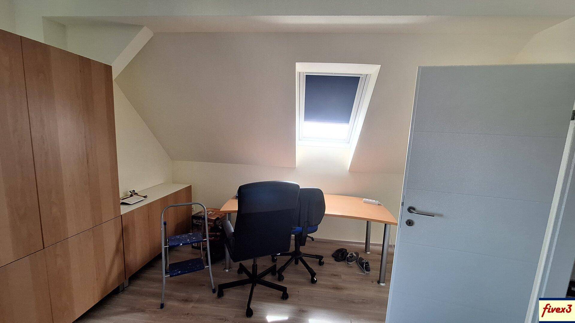 Dachgeschossbüro mit Schreibtisch, Bürostühlen und einem Dachfenster für Tageslicht.