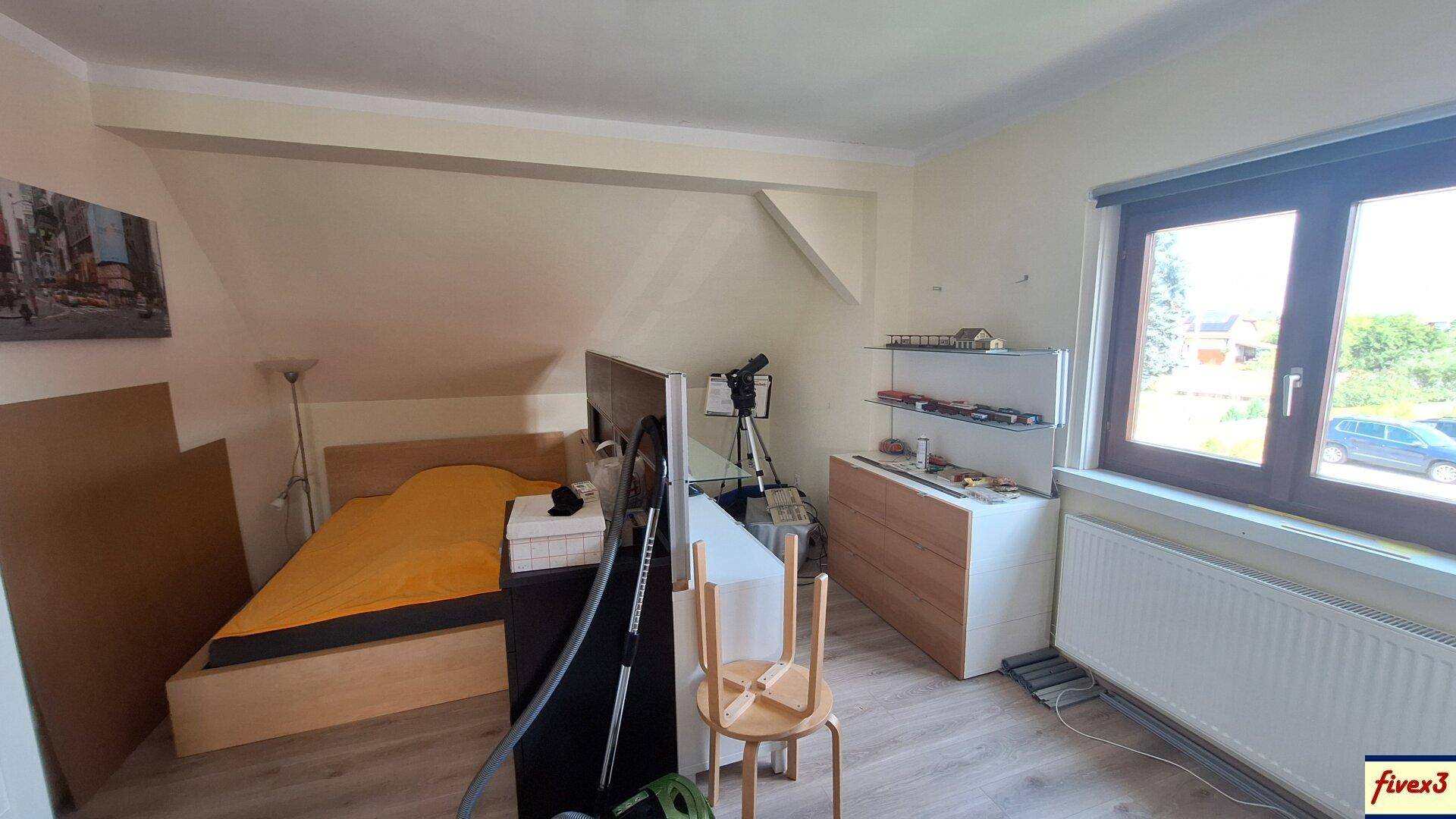 Dachgeschoss-Schlafzimmer mit Holzbett, Kommode und Fenster mit Ausblick.
