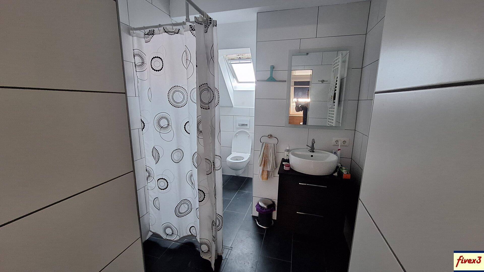 Modernes Badezimmer im Dachgeschoss mit Dusche, Waschbecken und Dachfenster.