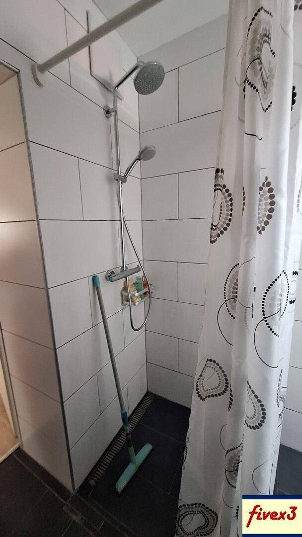 Duschbereich in einem modernen Badezimmer mit weißen Fliesen und Regendusche.