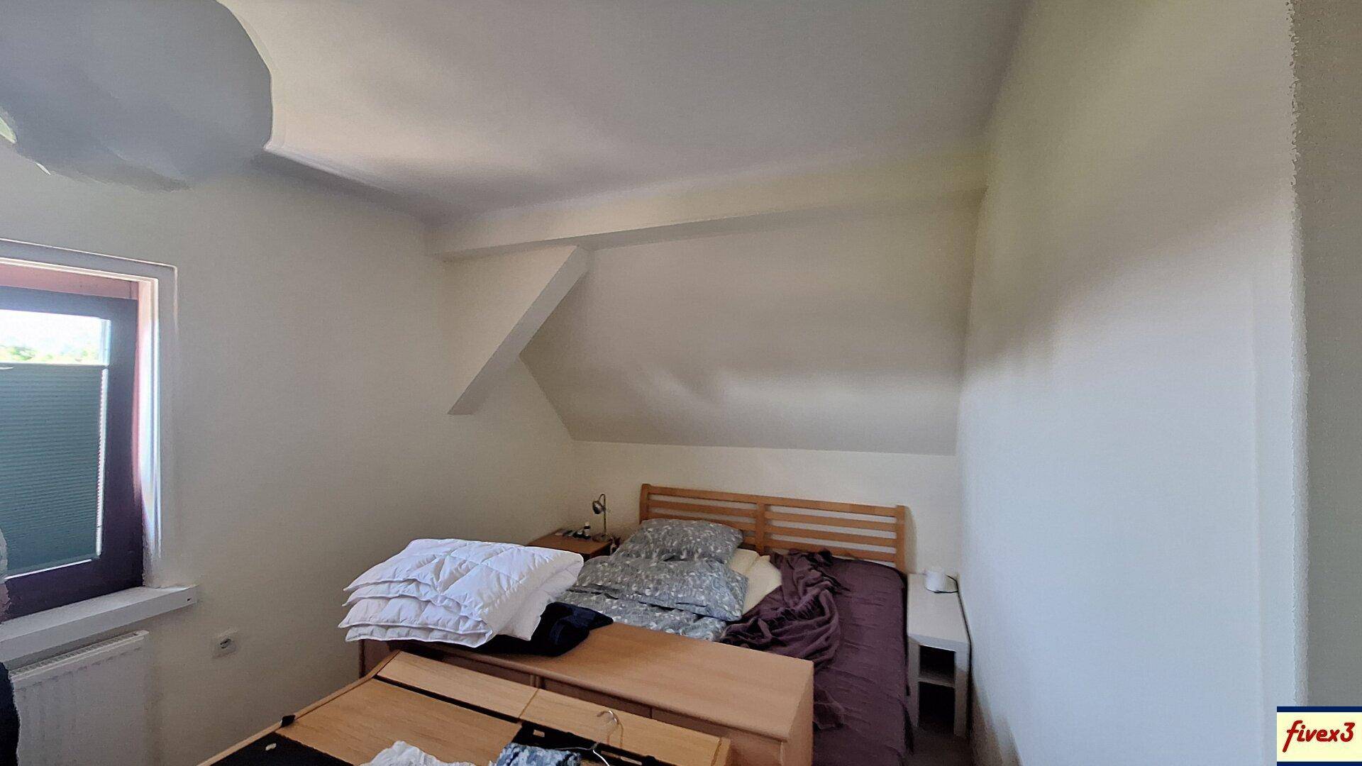 Helles Schlafzimmer im Dachgeschoss mit Holzbett und schrägen Wänden.